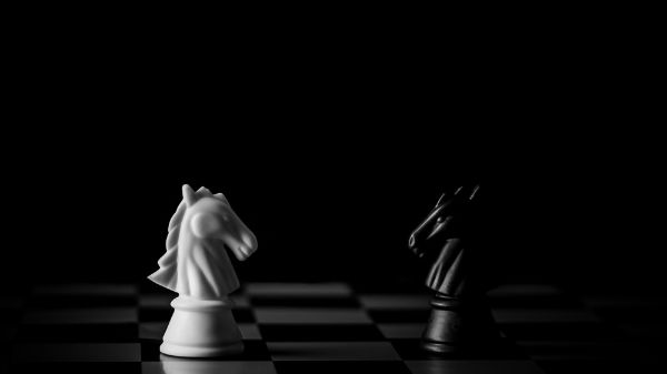 Picture of White and black horse chess encounter on a chessboard in the dark background